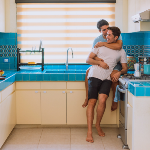 2 men standing in a blue and yellow kitchen with bright natural light embracing and smiling